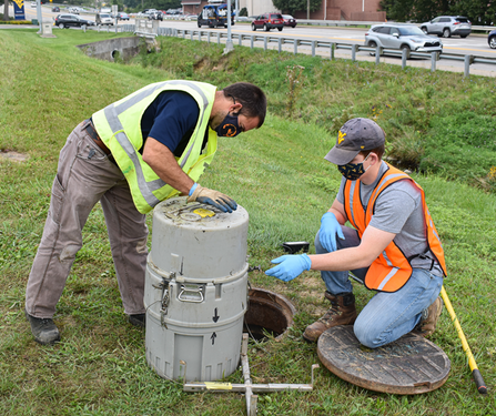 Two individuals work to open a sampler that was removed from a sewer manhole