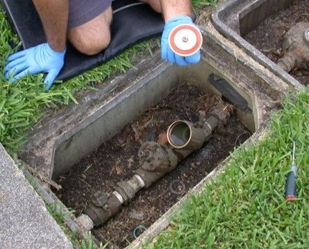 A person removes a cap from a pipe in the ground.