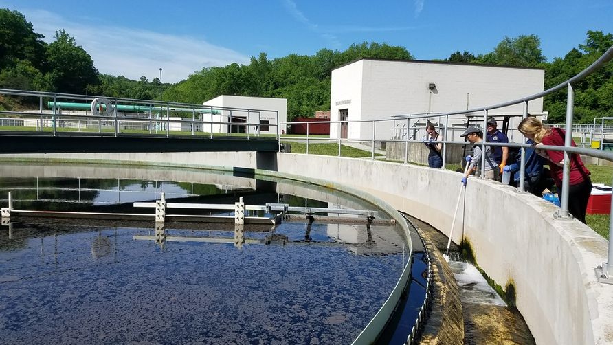 Students collect water from a large tank at a wastewater treatment plant.